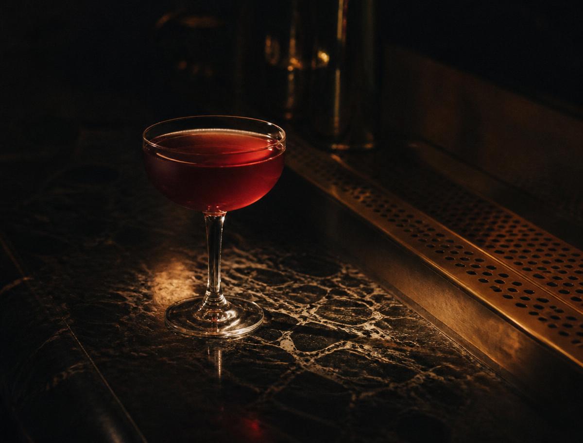 A deep red cocktail on a dark marble bar